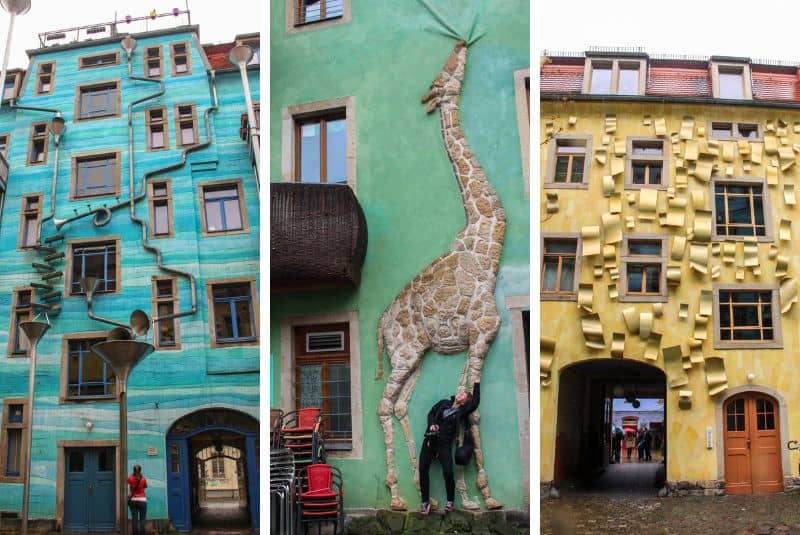 Three art house facades: A turquoise blue houses decorated with pipes and funnels; a green house with a stone giraffe stone sculpture; a yellow house with seemingly peeling elements. 