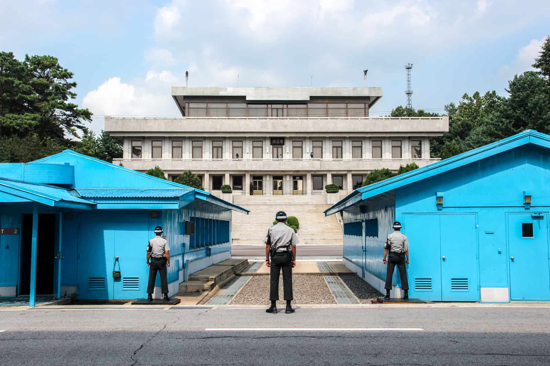 Three South Korean guards stand between two blue huts on the DMZ demiliterized zone facing North Korea. 