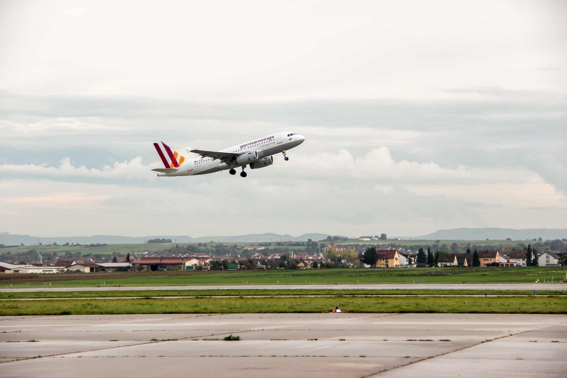 A white Germanwings logo plane midair during takeoff at an airport backed by a small village. 