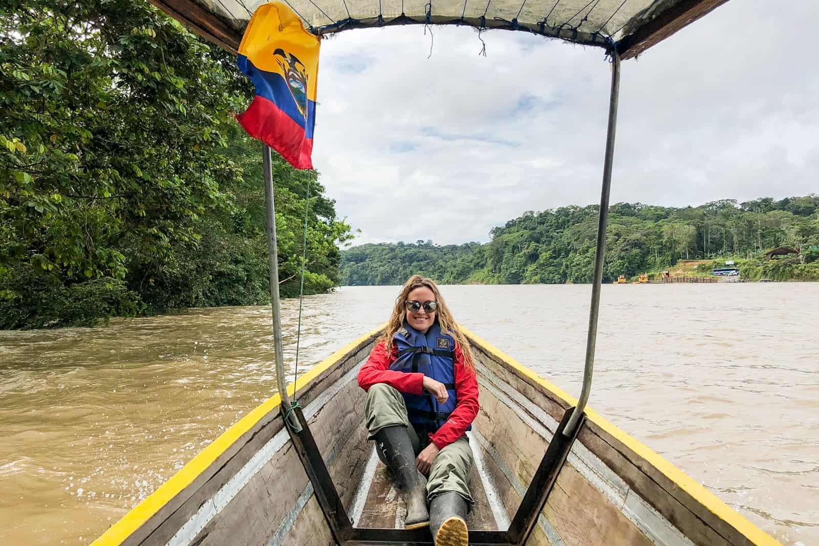 A woman sits in a longboat beneath a yellow, blue and red Ecuadorian flag on a trip on the Amazon River in Ecuador.