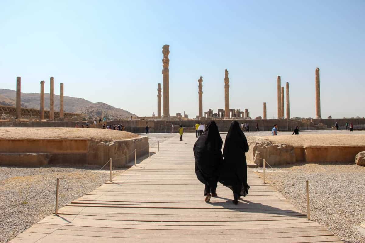 Two women in black conservative dress walking towards the ancient Persia ruins of Persepolis in Iran.