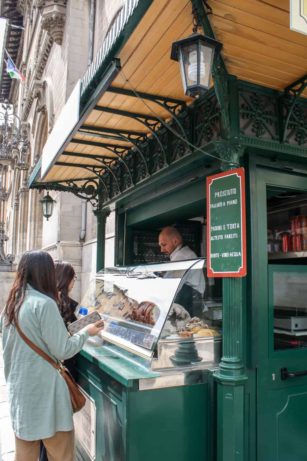 A man serves food to two customers from a green booth in Perugia, Italy. 