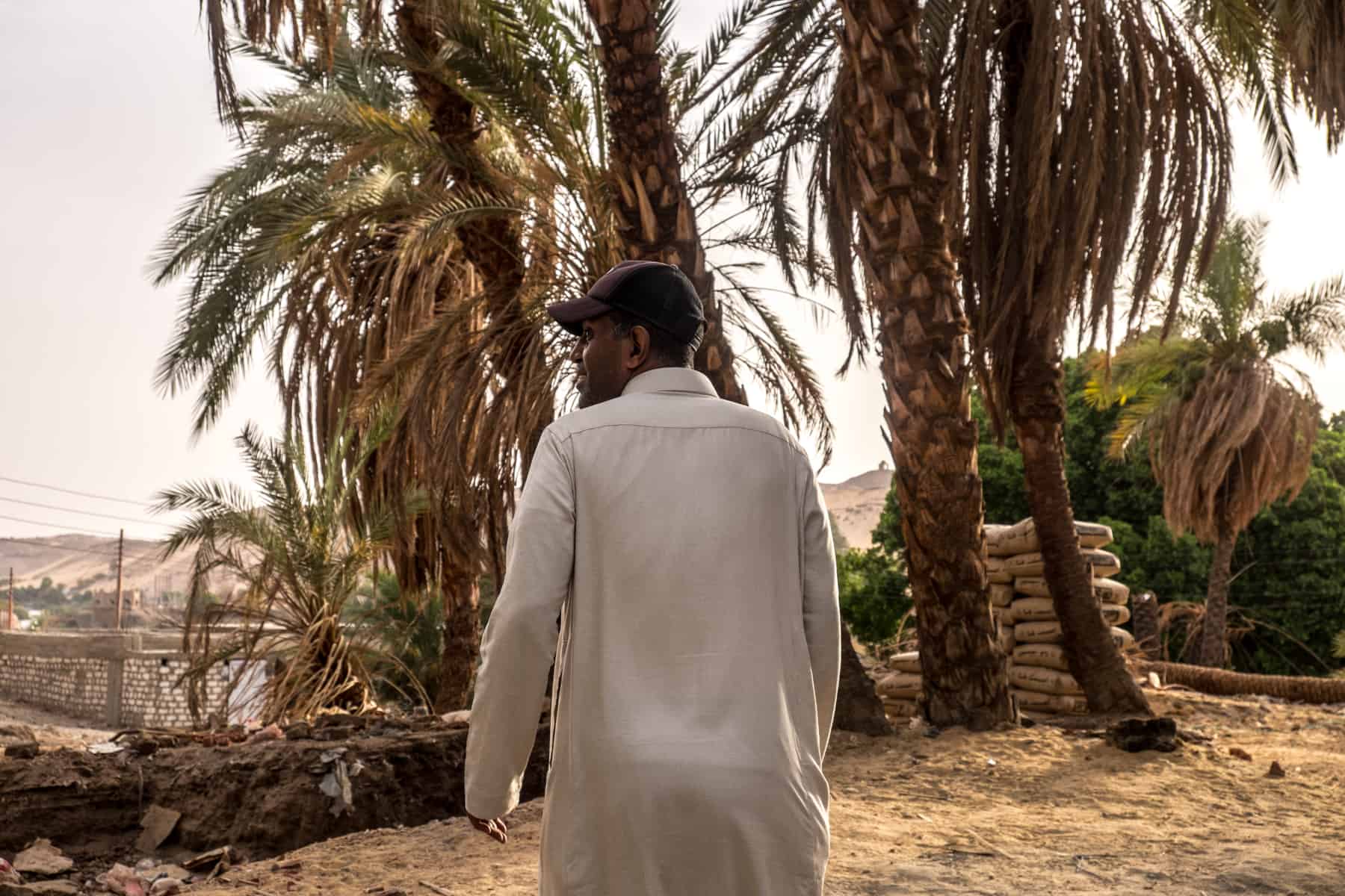 A Nubian man, dressed in a long white tunic in front of lush trees in his village on the banks of the Nile in Aswan, Egypt