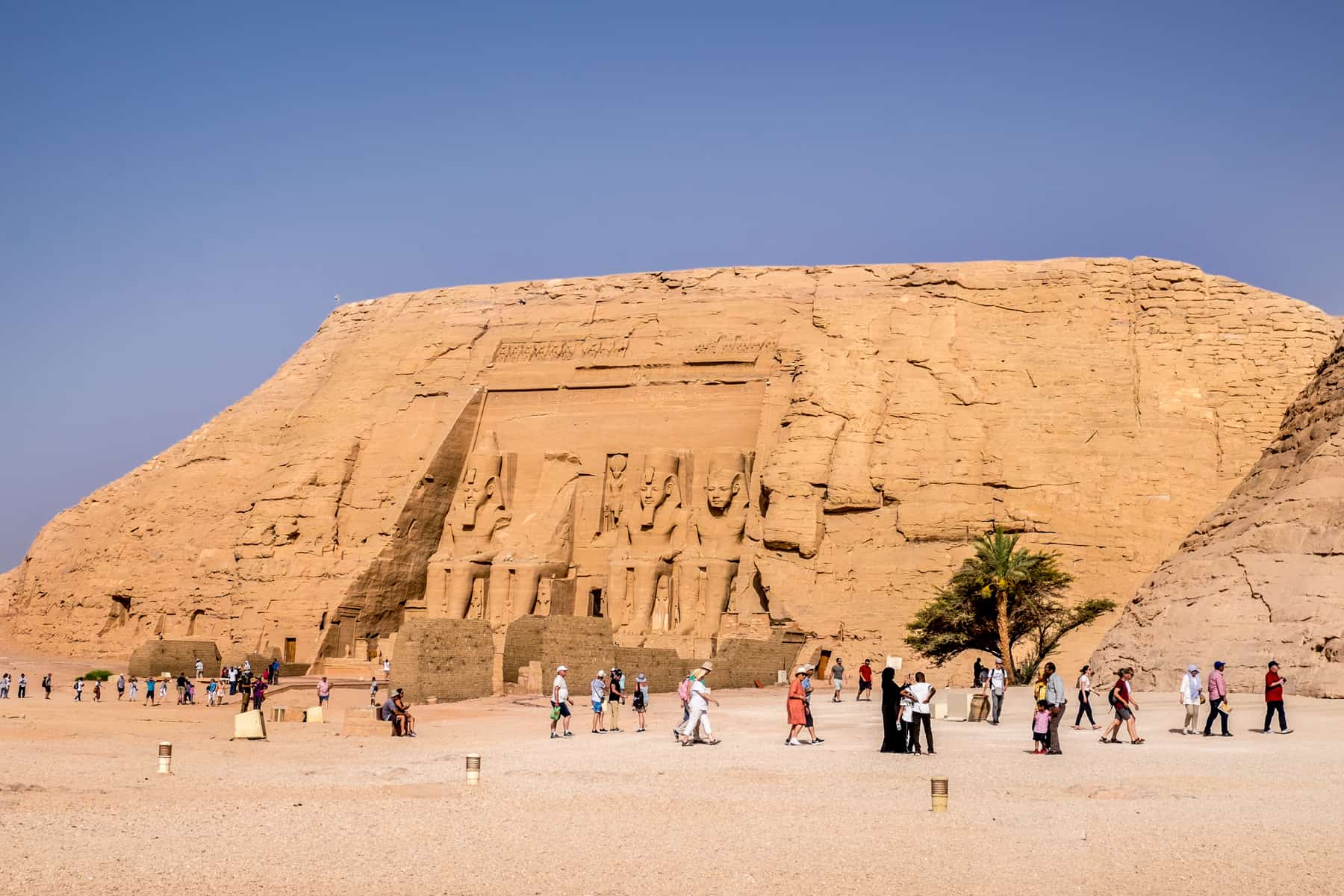 scattering of tourists look tiny next to the large mountain carved temple of Abu Simbel in Egypt that glows in the high sun