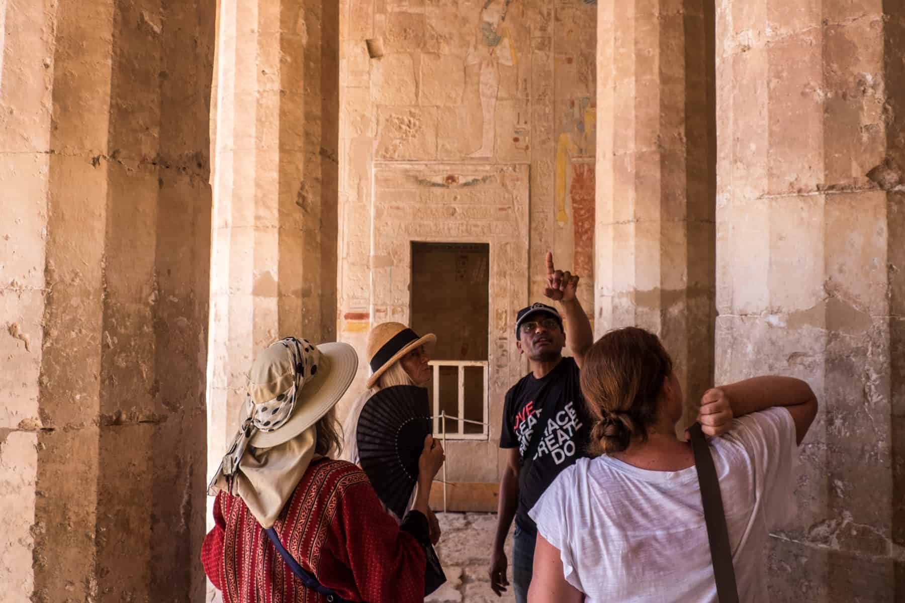 An Egyptian tour guide with three guests pointing to temple carvings