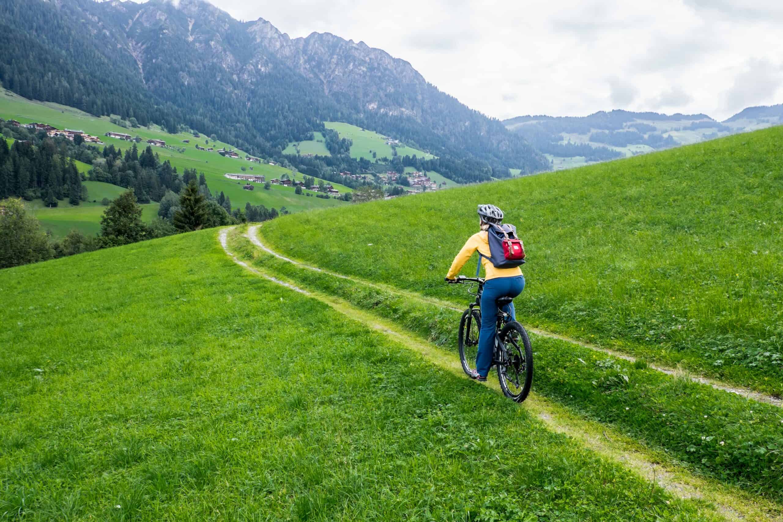 A woman in a yellow jacket and blue pants riding a bike on a alpine slope track.