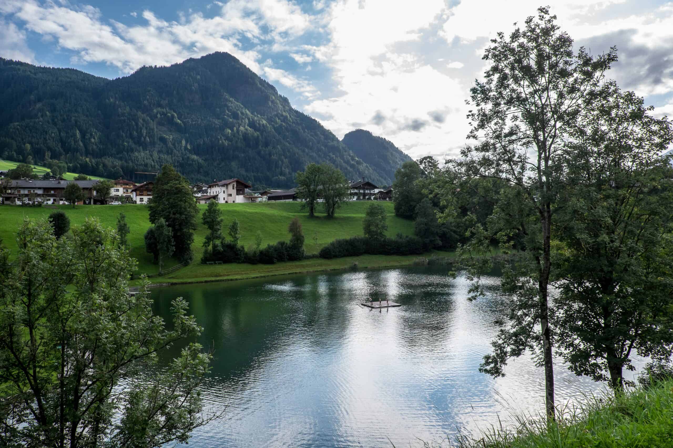 A small tree-lined lake in front of an alpine village in Austria. 