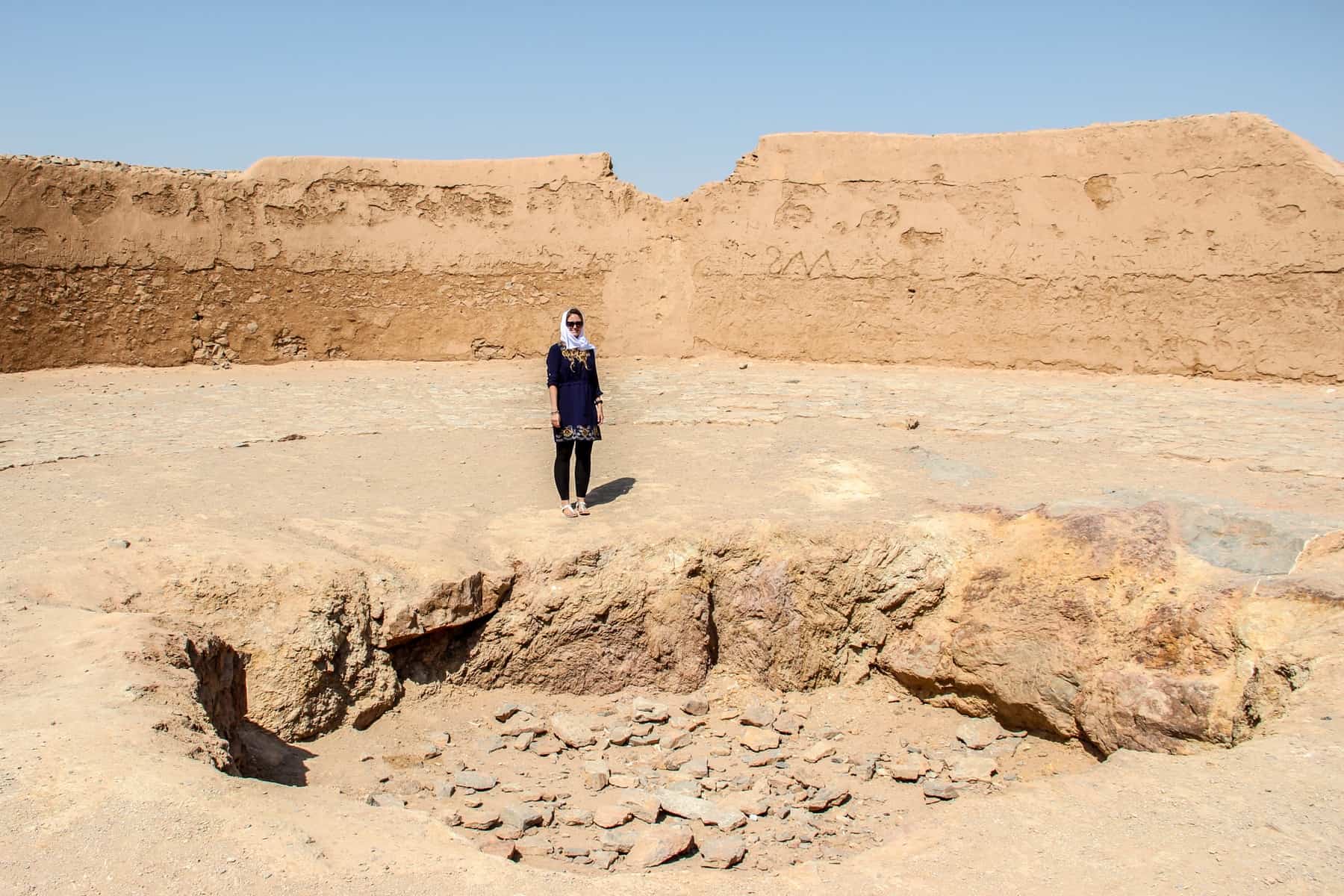 A woman standing next to a rock pit at the Zoroastrian Towers of Silence in Yazd on a trip to Iran.