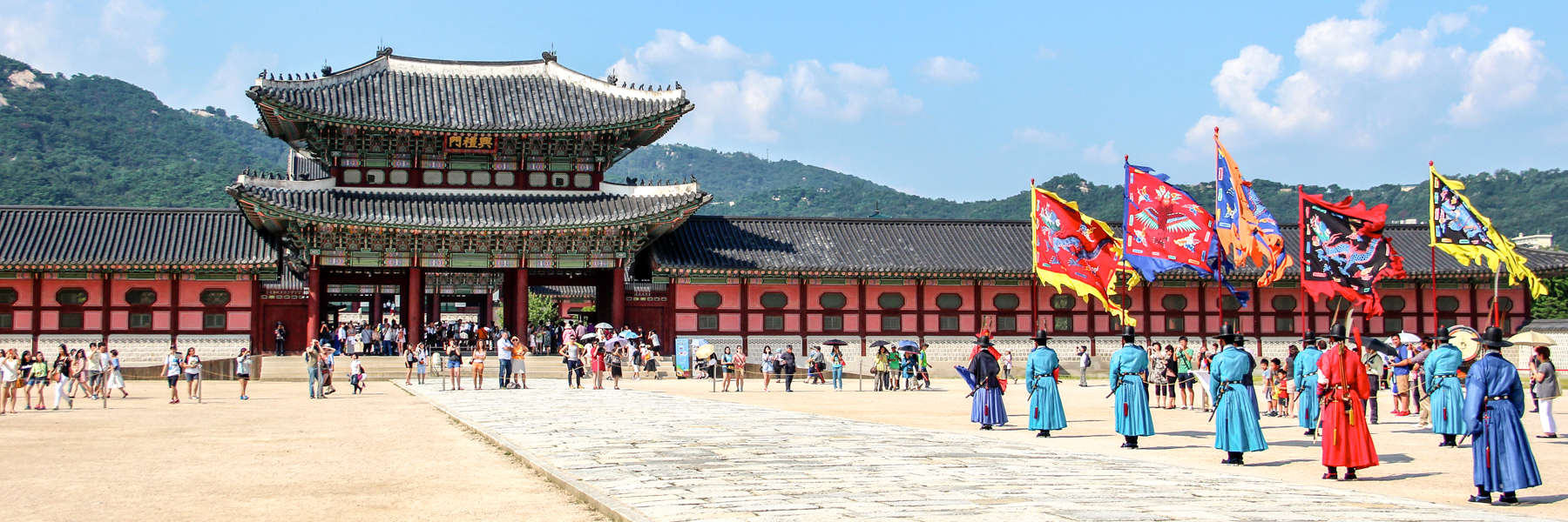 Performers in colourful traditional dress wave flags in front of the two-tier pagoda of Gyeongbokgung Palace in South Korea.