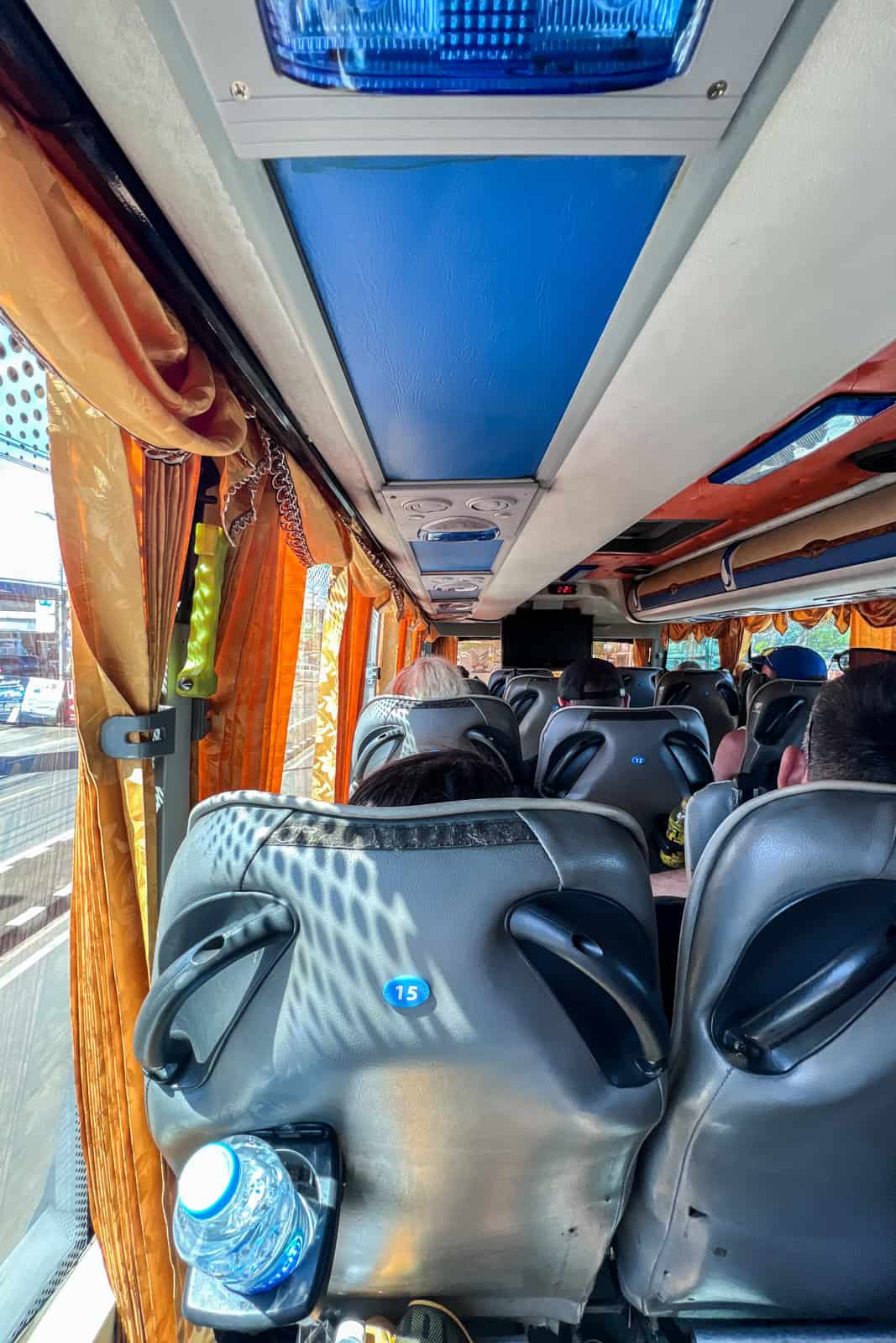 A bus in Thailand, with orange curtains, half full of people. 