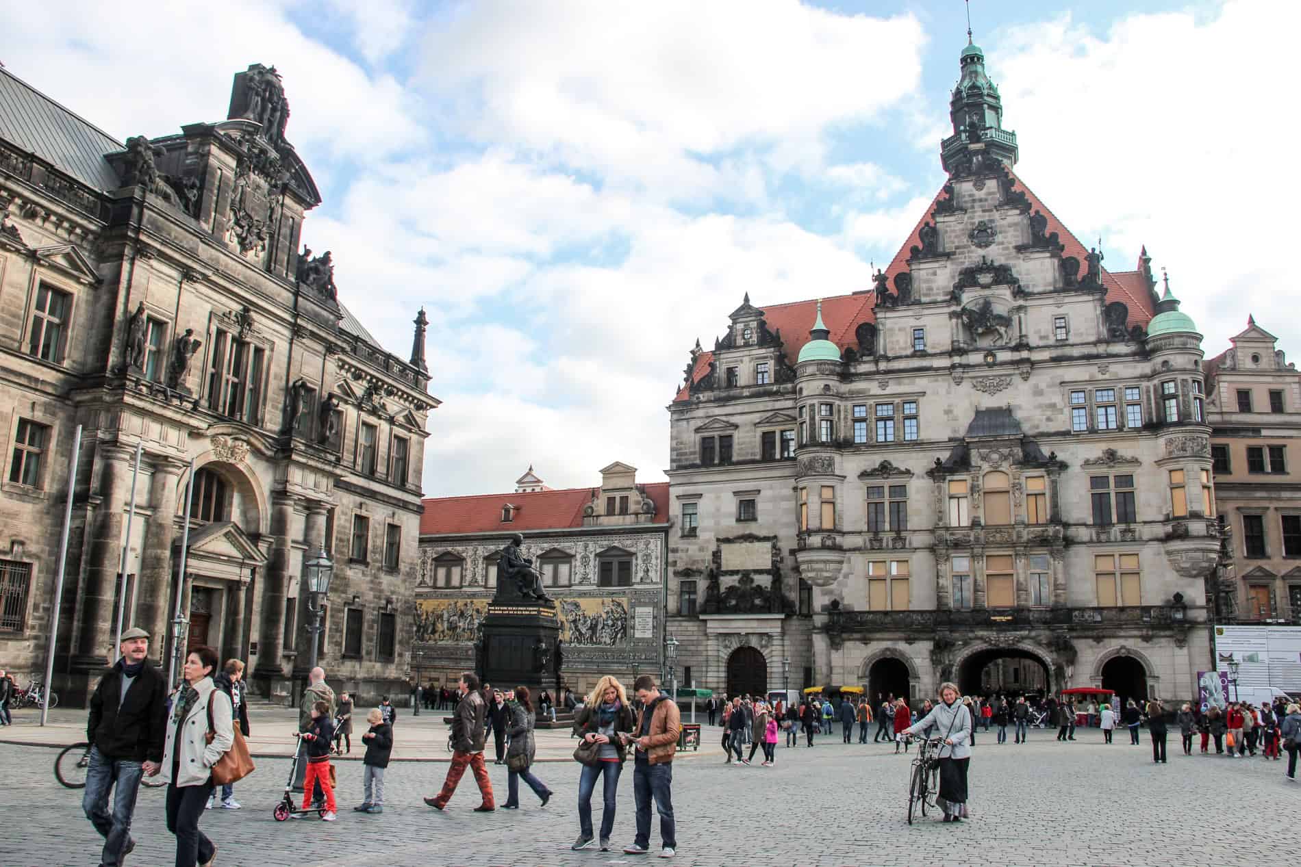 People walking through a Dresden city square surrounded by grand and weathered Renaissance buildings. 