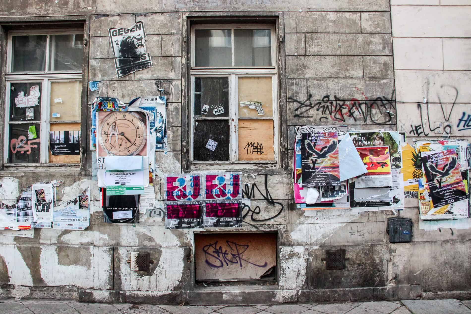 A stone wall with two windows, plastered with posters and art. 