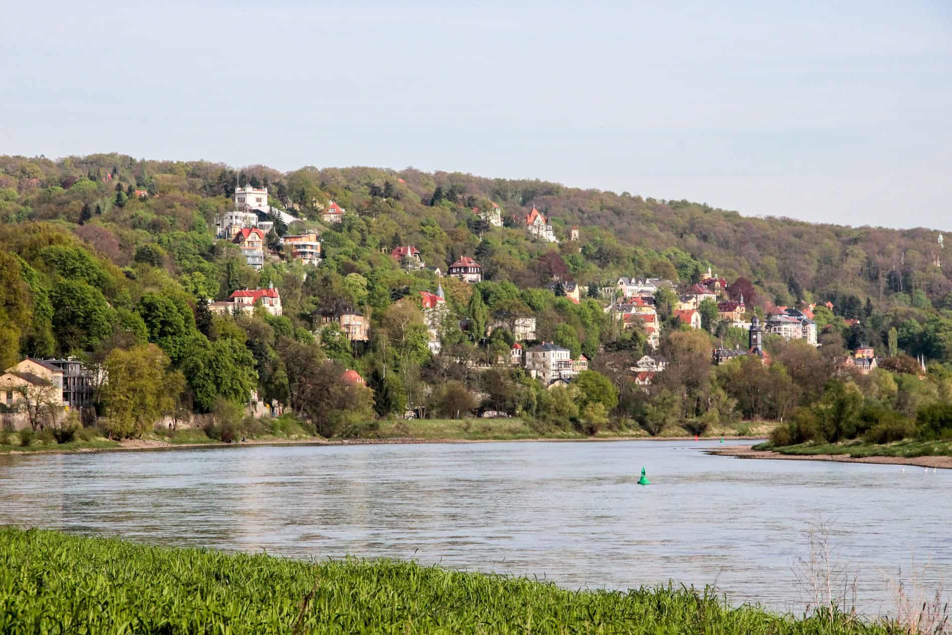 A cluster of houses with red roofs set in the green hills next to the Elbe River in Dresden. 