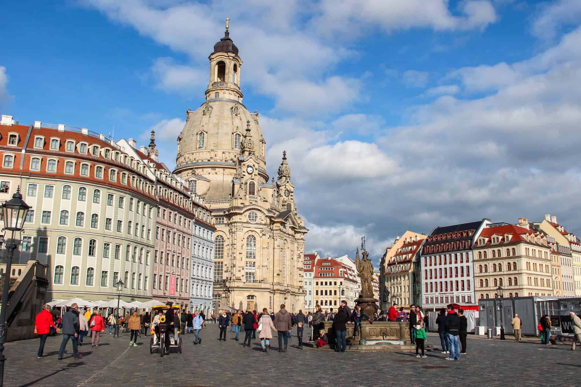 An ornate, domed and spired church building between rows of uniform, low-rise pastel painted apartment buildings. 