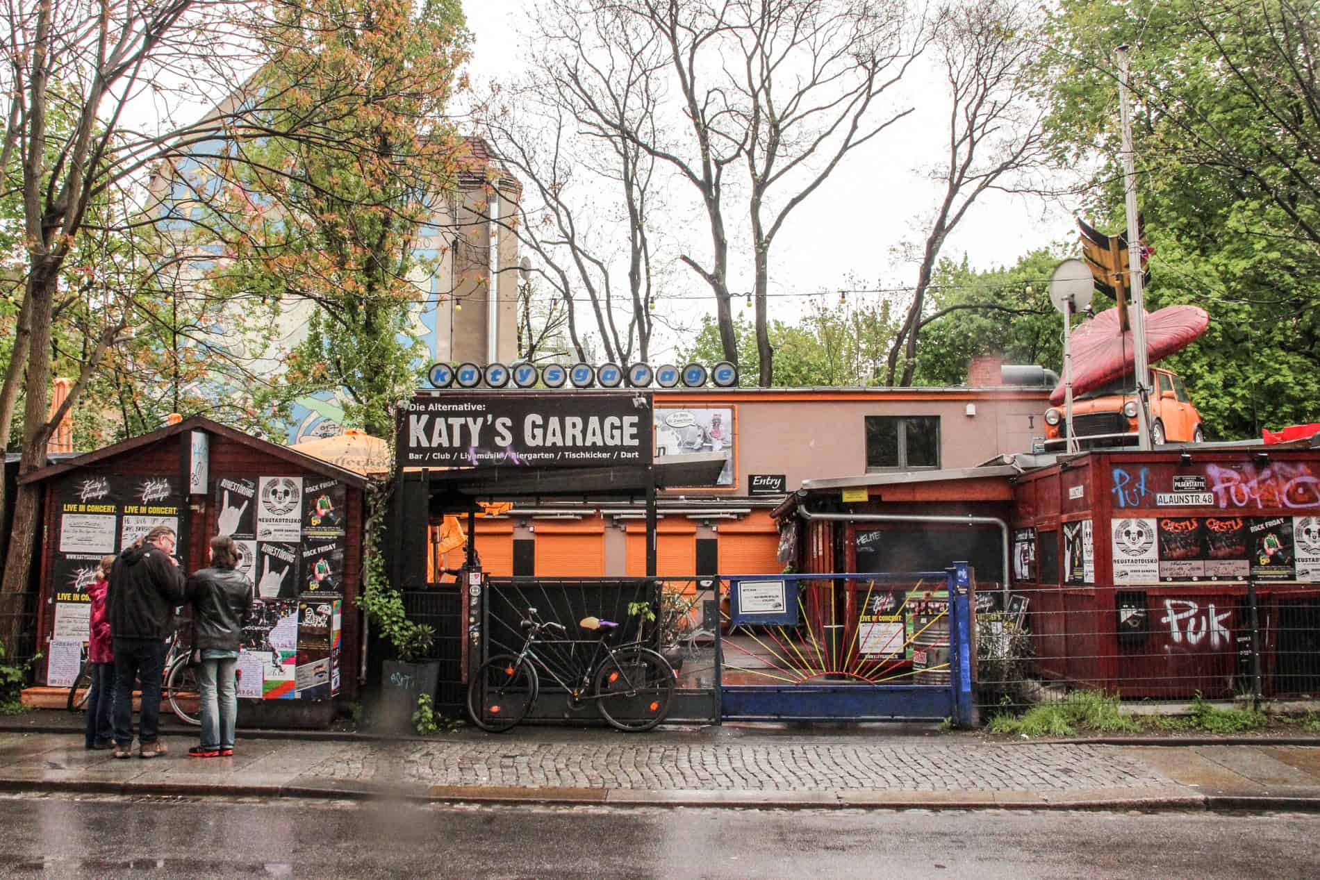 A low rise orange and red building with an orange mini car on the roof and a sign reading 'Katy's Garage'.