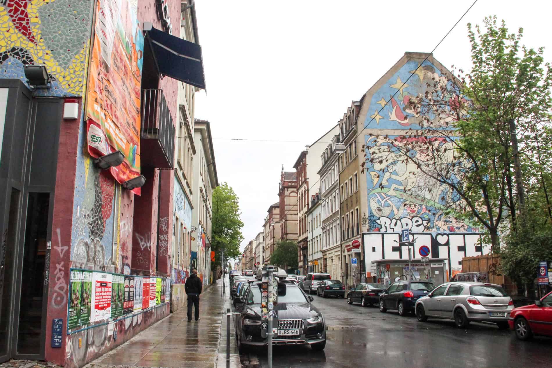 A car-lined street with street-art covered buildings. 