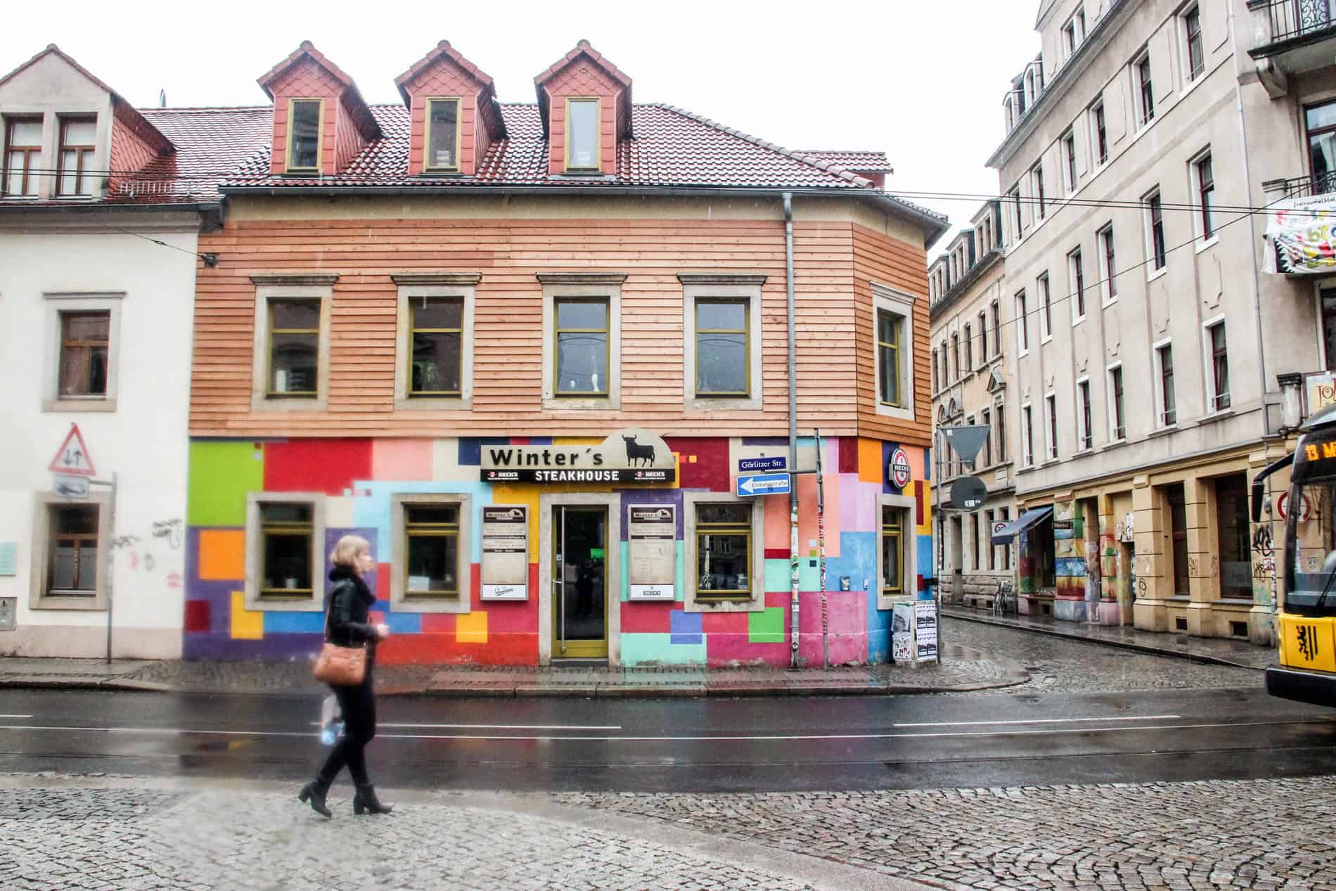 A woman walking past the facade of 'Winter's Steakhouse' in Dresden - the top is wooden panelled and the bottom is painted with multicoloured squares. 