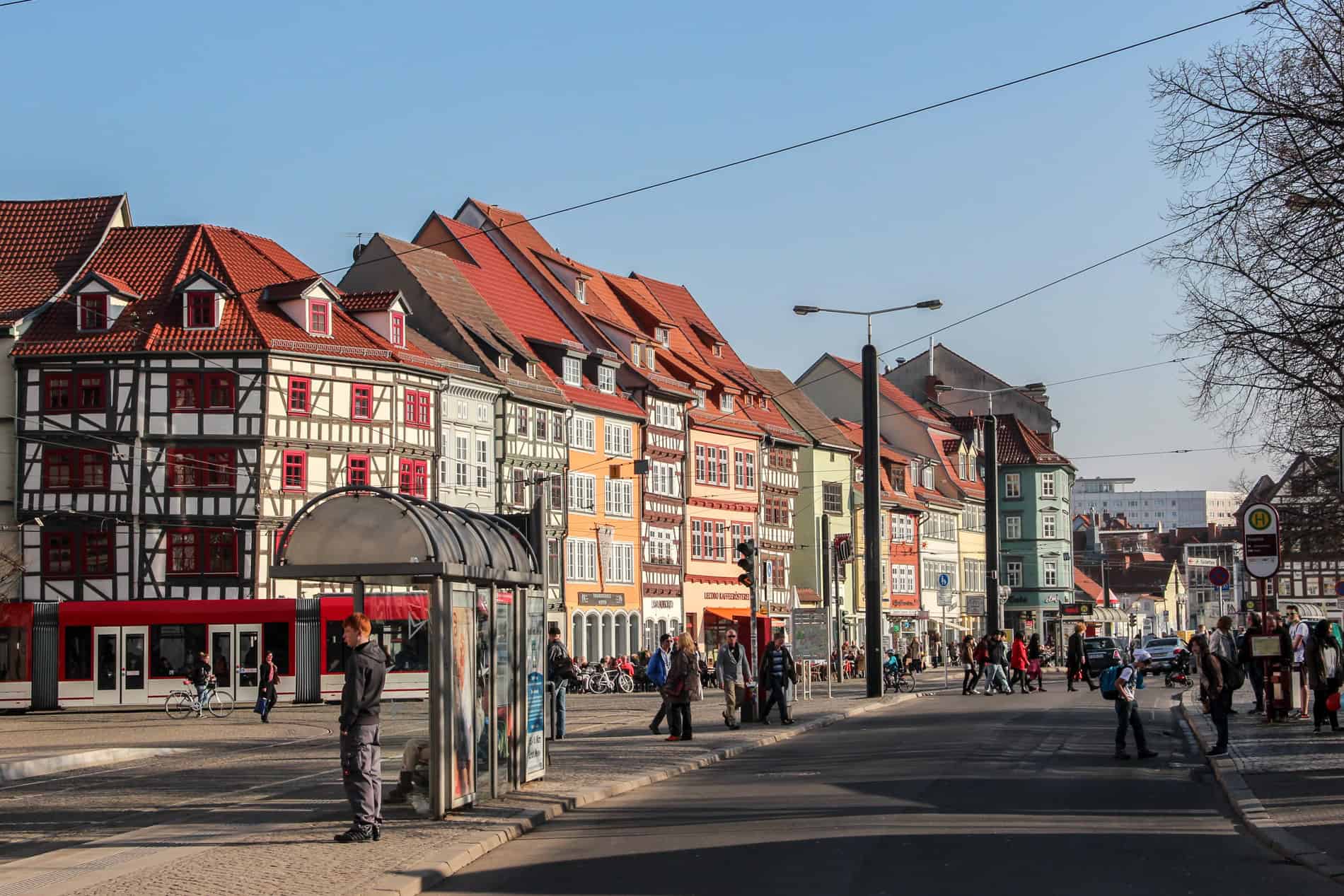 People walking in a road outside a curved row of Erfurt's colourful restored Renaissance buildings.