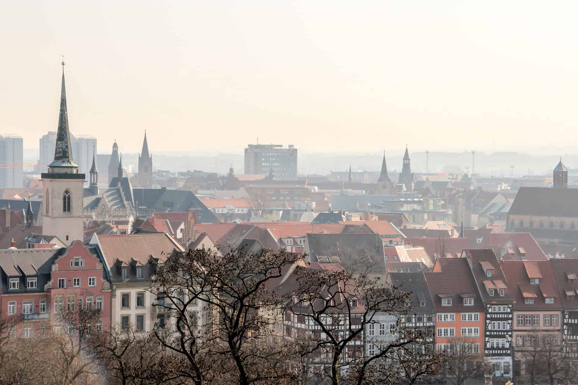 Elevated view of red rooftops and church spires of Erfurt city, shrouded in a light fog.