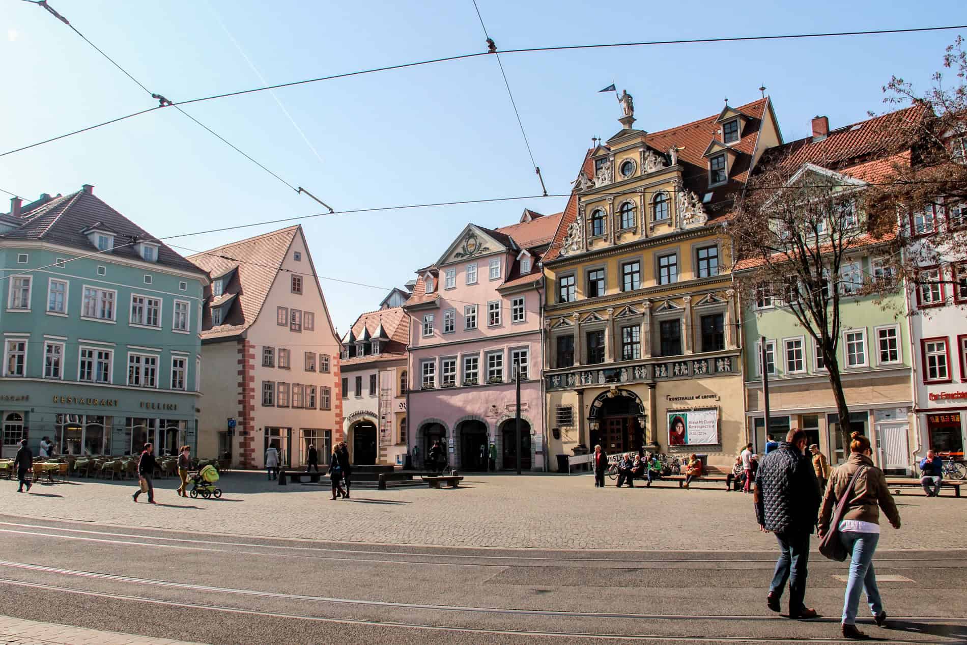 People walking in Erfurt's Fischmarkt Square with restored pastel painted Renaissance buildings.