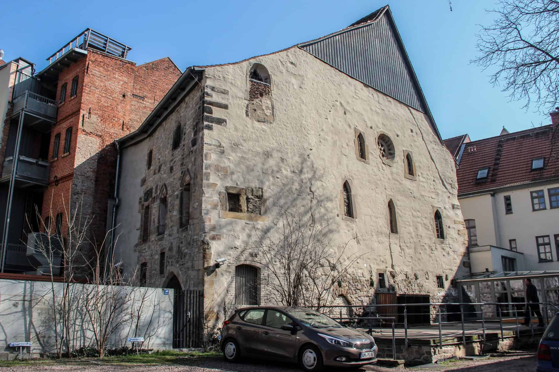 An old stone building Synagogue building in Erfurt, with a black pointed roof and sporadically-placed windows. 