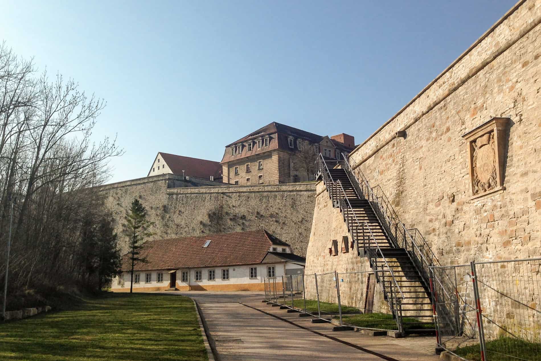 The imposing golden stone walls and metal staircase of Erfurt's fortress, Zitadelle Petersberg. 